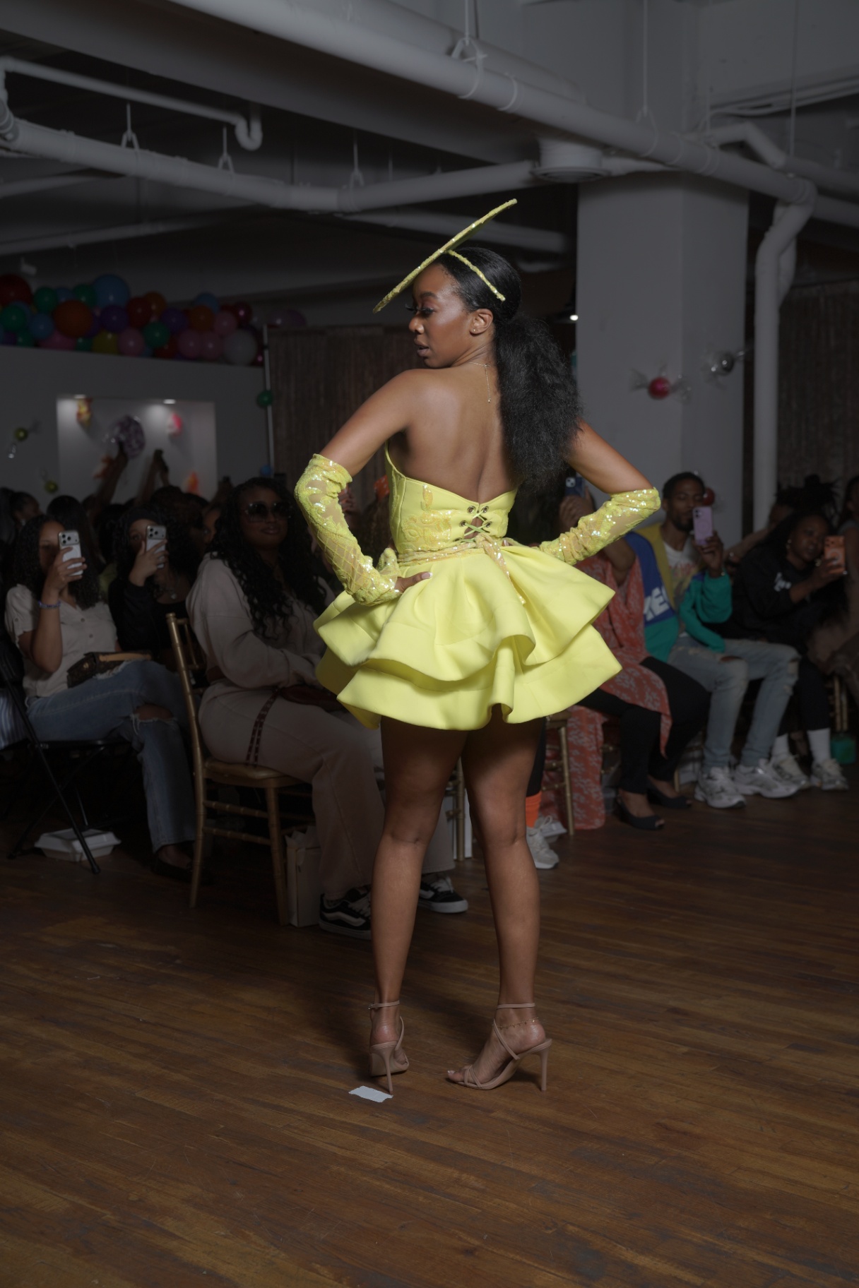 Model in a yellow ruffled mini dress with matching beret from behind