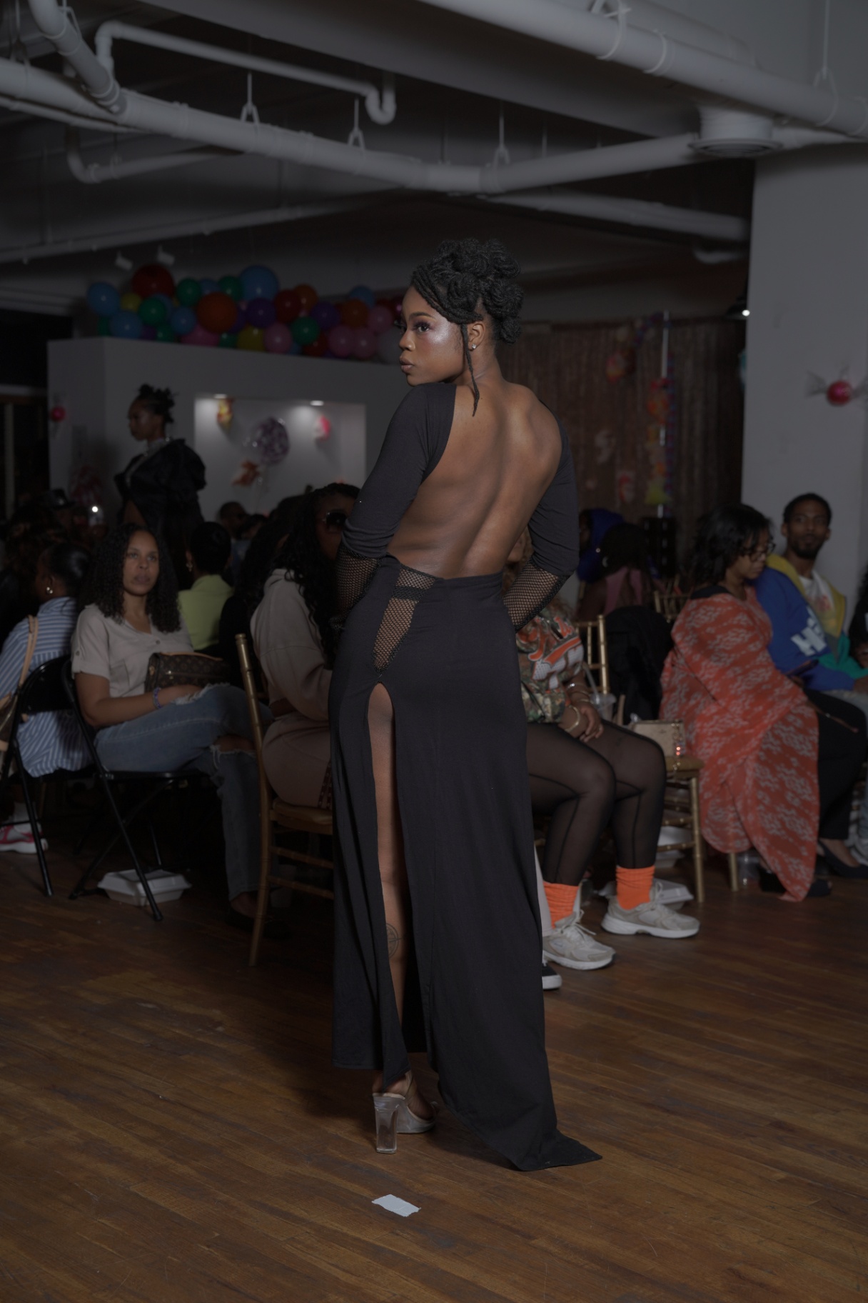 Model in a black backless gown with side cutouts walking away on the runway