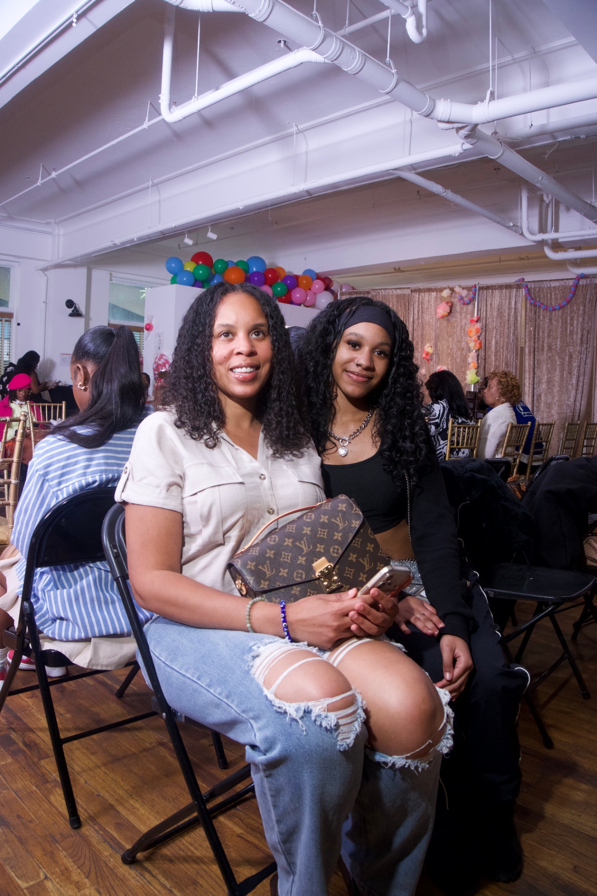 Two guests seated front row with a Louis Vuitton bag