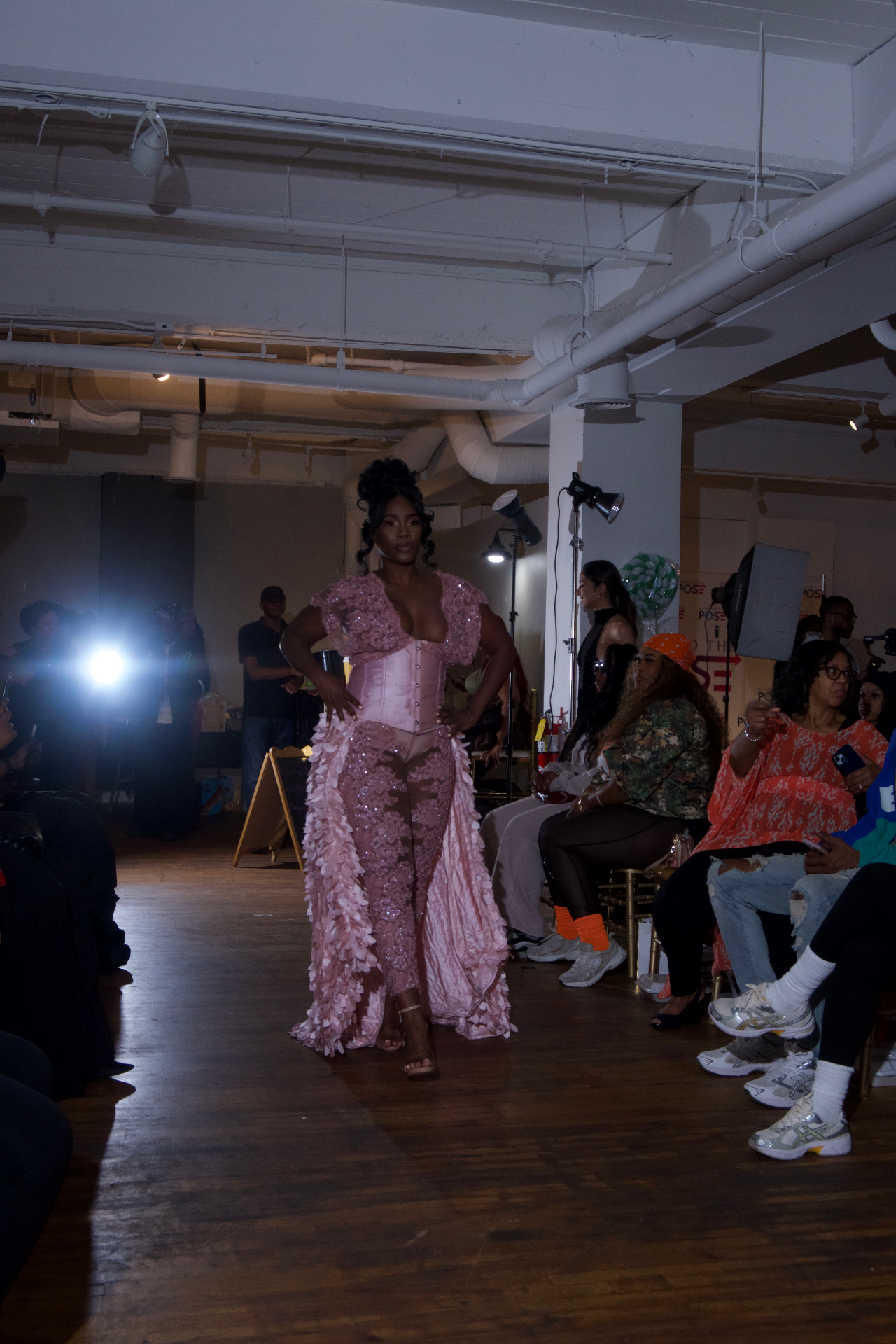 Model in a pink corset gown with feathered train under stage lights