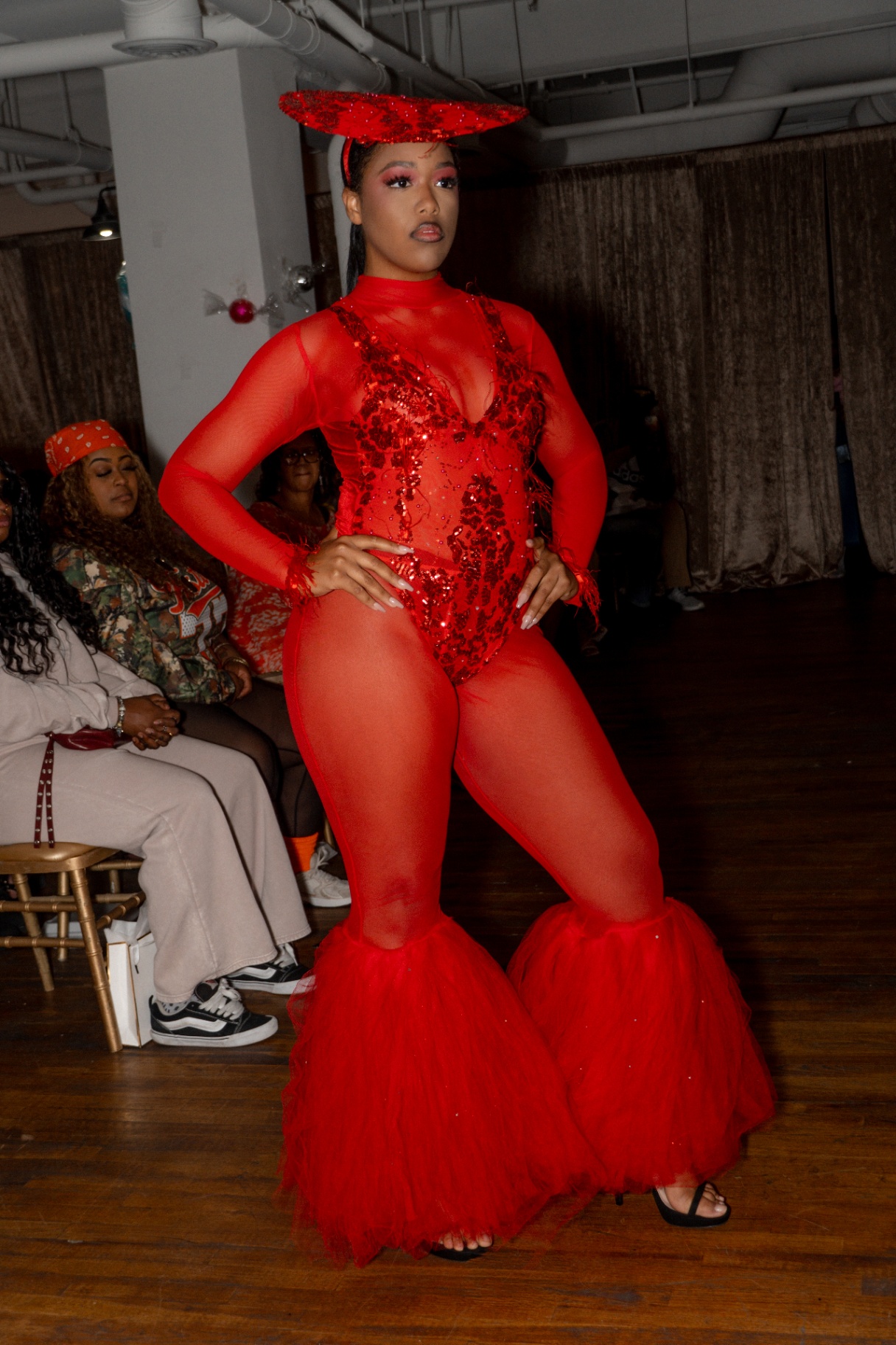 Model in a red sheer bodysuit with tulle bell cuffs and matching halo hat