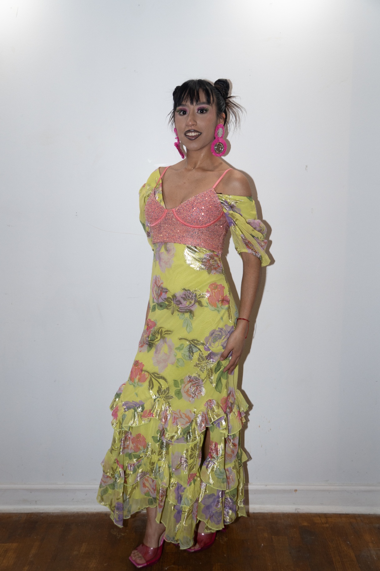 Model in a yellow floral ruffled gown with pink earrings posing backstage