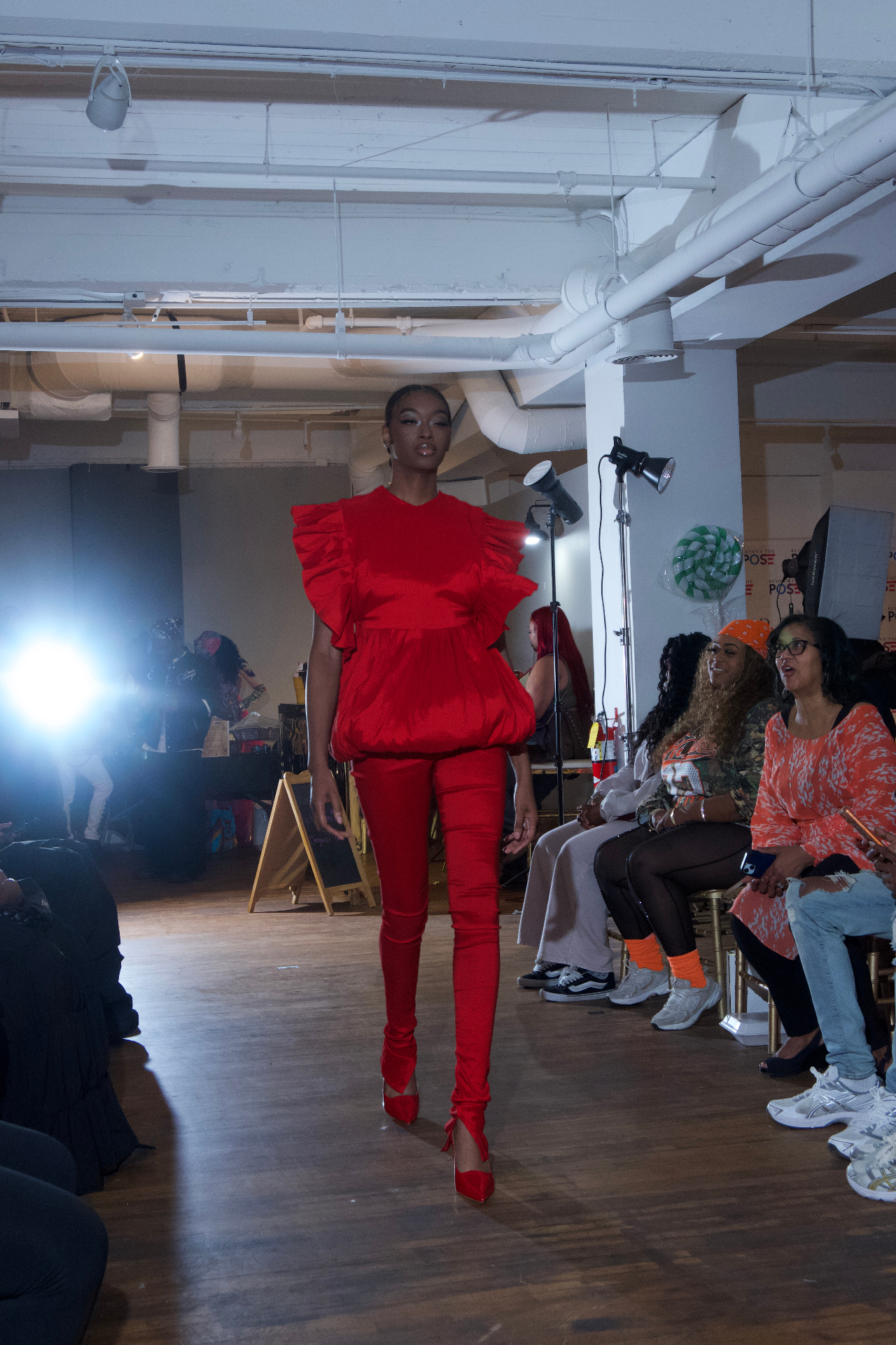 Model in a red ruffled top and red pants walking past seated guests
