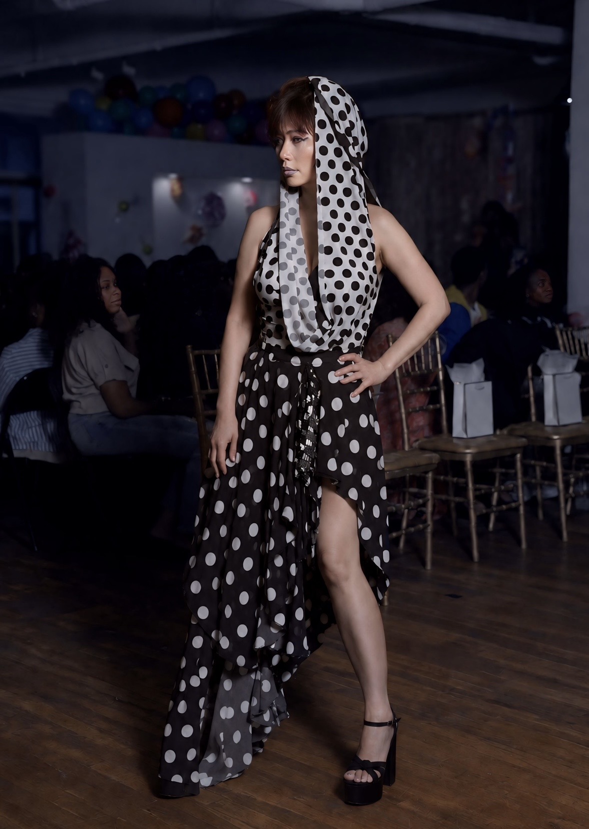 Model in a black-and-white polka-dot hooded halter dress on the runway