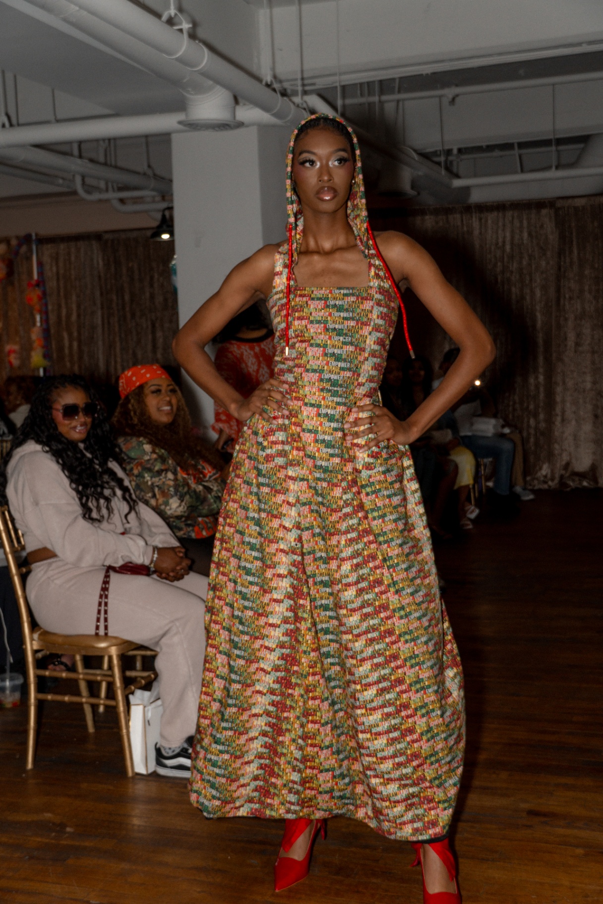Model in a printed 'Empower' hooded floor-length dress with red heels