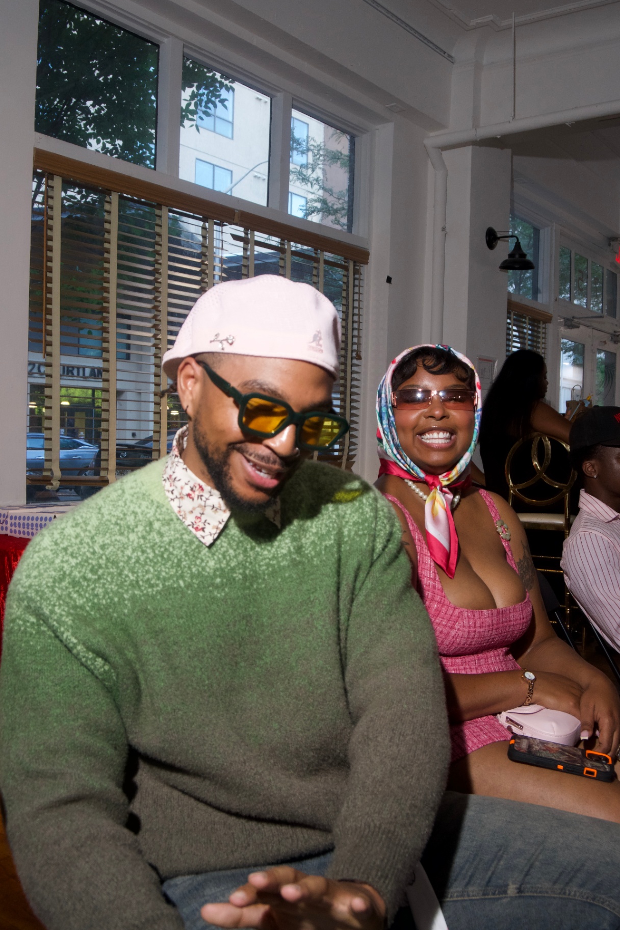 Couple seated front row, one in a green sweater and one in a pink dress