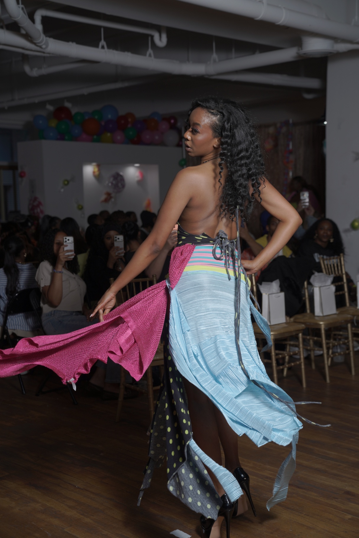 Model in a striped halter dress with pink and blue draped panels walking the runway