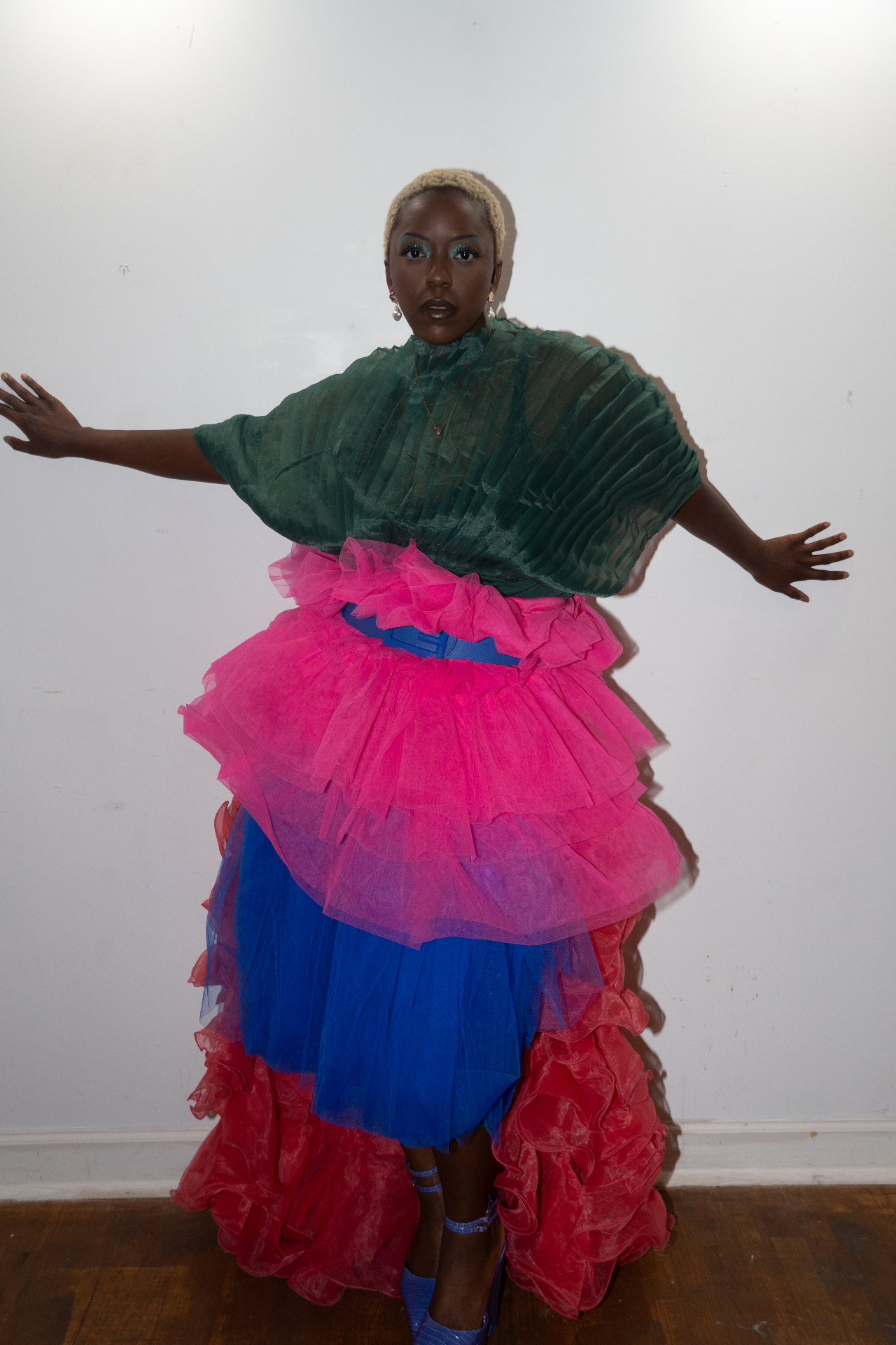 Model in a tiered green, pink, blue and red tulle gown with arms outstretched